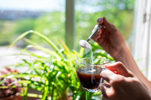 Woman holding a cup of coffee in her hand while pouring sugar into it.