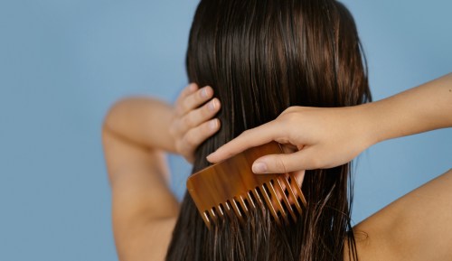 A woman with long dark hair is combing her wet hair with a comb. Her hand is captured close-up in motion as she brushes her hair, capturing the moment of self-care and grooming.