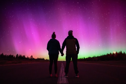 Couple holding hands under the Aurora Borealis ,