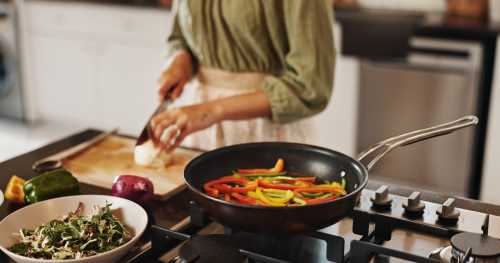 Close up of person in green long sleeve shirt and tan pants chopping vegetables at their kitchen island while sauteeing bell peppers in a cast iron skillet, trying to eat plant sterols for cholesterol and overall health