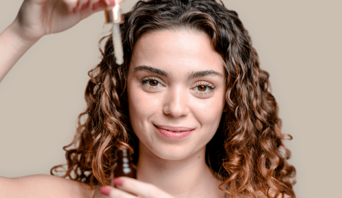 Young woman smiling while holding a bottle with plant-based oils for her skin care routine.