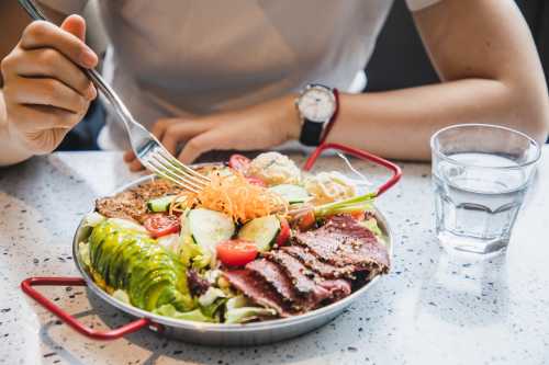 a person sits at a table enjoying healthy fruit, vegetable and meat salad with balance nutrition