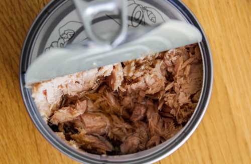 a can of tuna sits half-opened on a wood surface