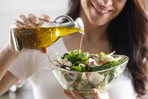 Young woman, smiling, pouring olive oil in to a salad in a glass bowl.