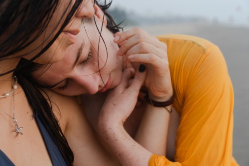 Two women embrace in an emotional hug on a beach.