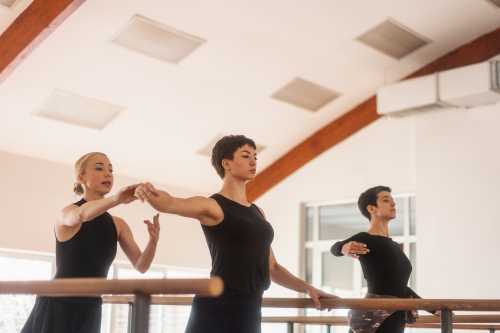 Two young women practicing ballet with a teacher in the dance hall.