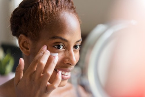 Beautiful woman looking in mirror, applying Elizabeth Arden skincare lotion to face