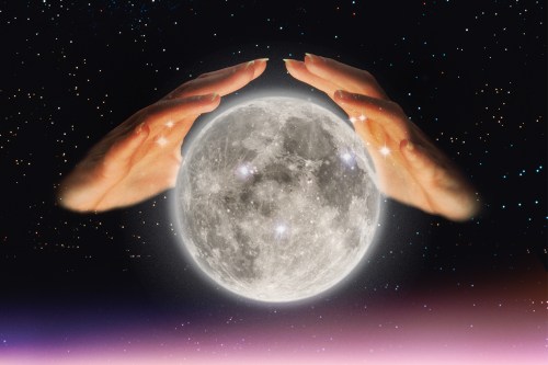 Two hands are seen over a large full moon.