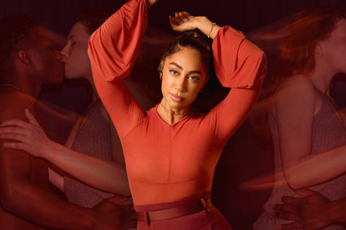 sex educator and MasterClass Instructor Shan Boodram posing for a portrait in front of a red background that shows couples kissing in honor of valentine's day