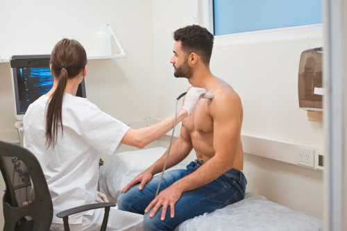 Doctor doing an ultrasound on man's chest in an examination room.