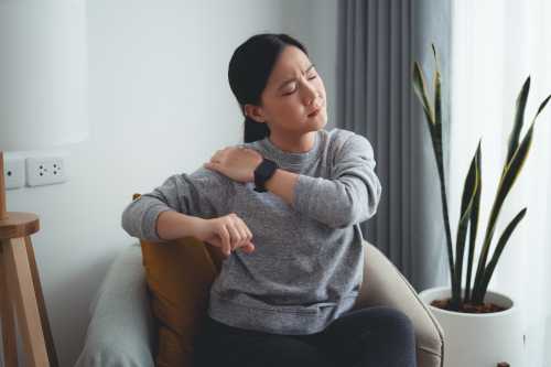 woman in grey sweatshirt sitting on chair and experiencing arm and back pain