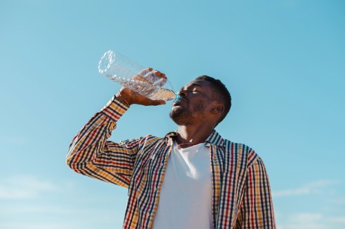 man in a white shirt and multicolored collared shirt drinking water from a plastic bottle