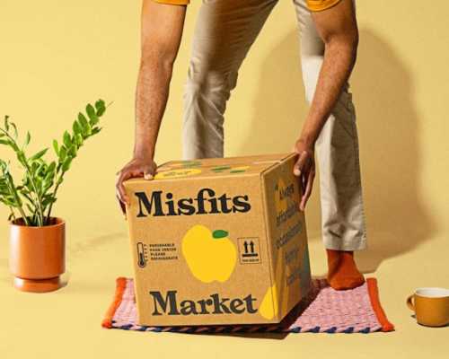 a man grabs a branded grocery box off of a red doormat, on a yellow background