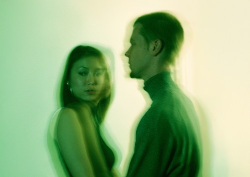 blurred image of a couple standing in front of each other but looking away against a green background to display signs your body is rejecting someone in a relationship