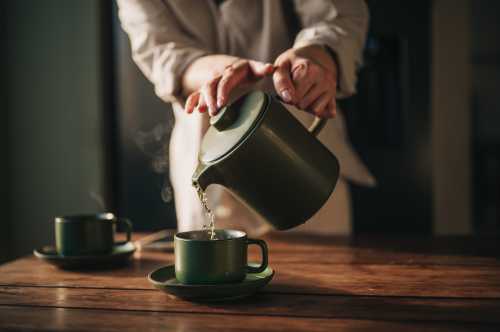 Tea is poured from a green teapot into matching mugs