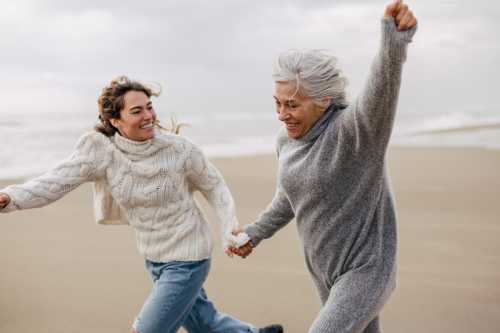 An older woman and younger women are seen running on a beach.