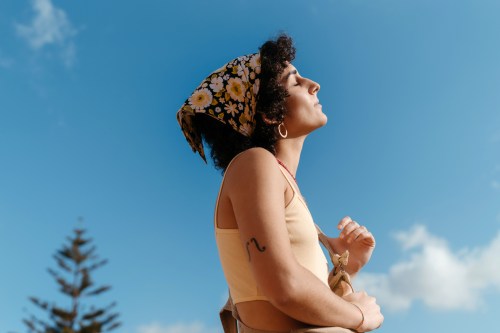 Portrait of a young woman enjoying a sunny day, wearing a headscarf, with the blue sky behind.