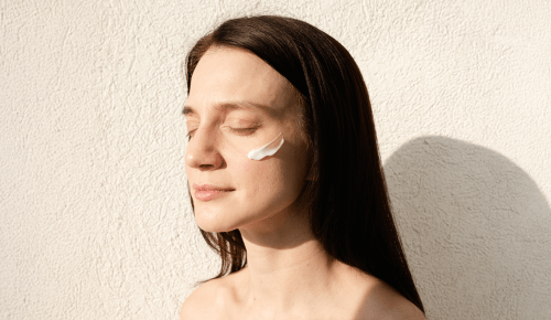 Side view portrait of woman posing with closed eyes with true botanicals chebula cream on her cheek in sunny day