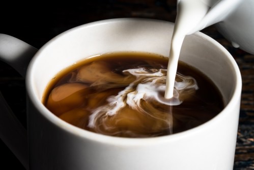 close up shot pouring creamer into a cup of coffee