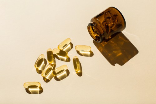 Omega 3 fish oil capsules and a glass bottle on a beige background.