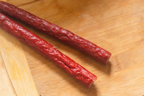 Two sticks of jerky sit on a wood cutting board.