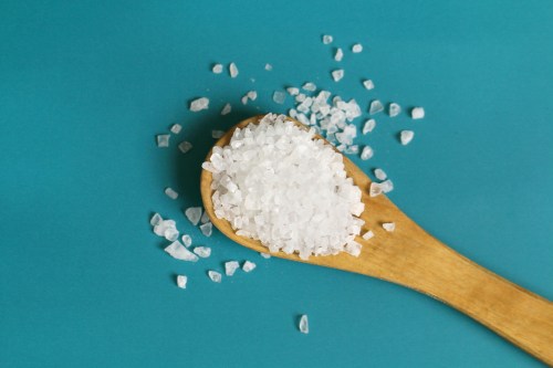 Coarse salt crystals on a blue table held in a wooden spoon with more sea salt.