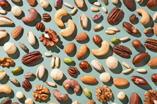 Various Mixed Nuts Include Almonds, Brazil Nuts, Cashews, Hazelnuts, Macadamia Nuts, Pecans, Pine Nuts, Pistachios, Walnuts Flat Lay on Green Background Directly Above View.