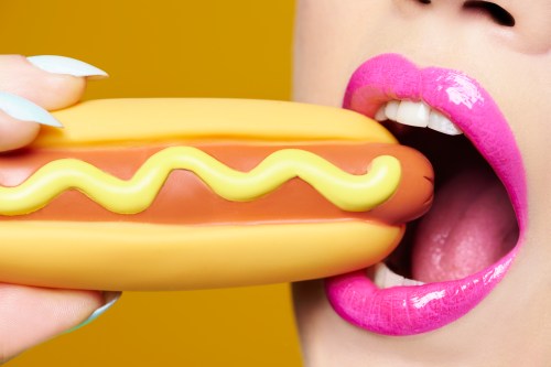 woman wearing pink lipstick about to bite into a plastic hotdog