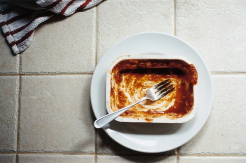 Empty microwave meal sits on a white ceramic plate on a white tile countertop.