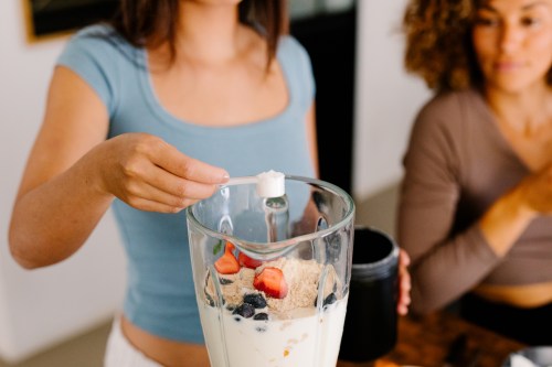 A mid-frame of an anonymous woman adding creatine powder into a blender to make a shake, incorporating supplements as part of a nutritious morning meal.