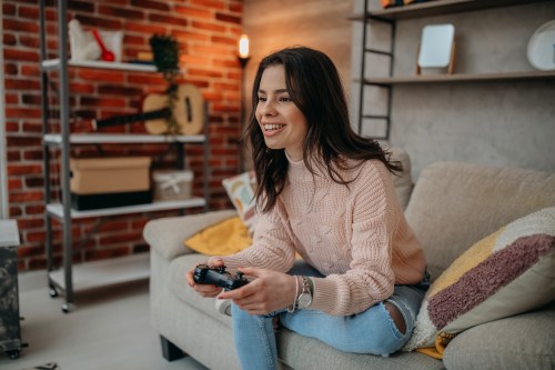 woman in light pink sweatshirt sitting on couch and holding a video game controller