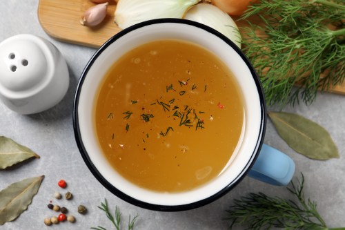 Hot delicious bouillon in cup and ingredients on light grey table