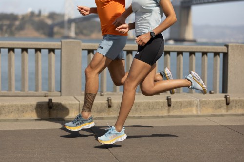 Two runners wearing Hoka Bondi 8 run next to the water.