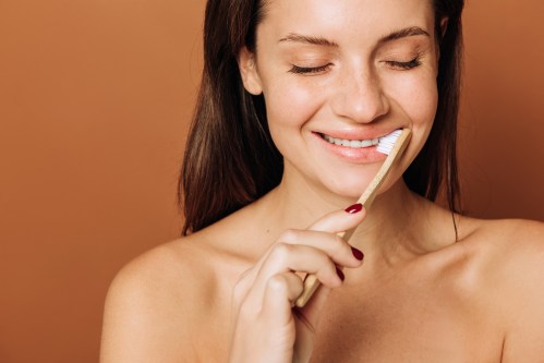 close up of woman smiling while brushing her teeth, wondering how often should I change my toothbrush