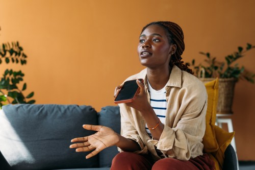 person wearing a tan button down shirt on top of black and white striped shirt and red pants sitting on their coach in their living room talking on the phone and learning how to deal with a narcissistic parent