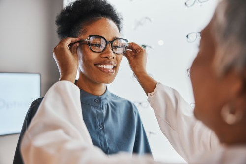 close up of person with short curly black hair in a blue long sleeve button down shirt getting a vision exam and trying on glasses at the eye doctor to reduce dementia risk in 40s