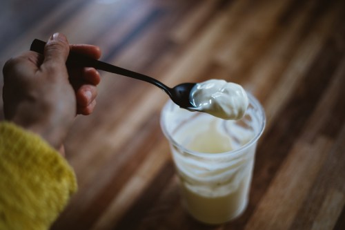 Yogurt in a plastic container and a woman's hand holding a spoon of yogurt
