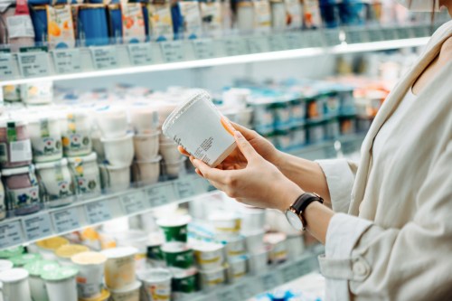 Cropped shot of young woman shopping in the dairy section of a supermarket. She is reading the nutrition label on a container of fresh organic healthy natural yoghurt