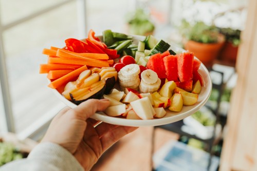 Plate of many various greens and fruits held by a hand with body off-camera
