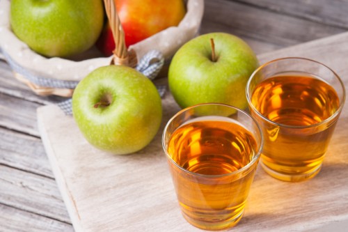 Photography of a apple juice in glasses and apples in a wicker basket on wooden table