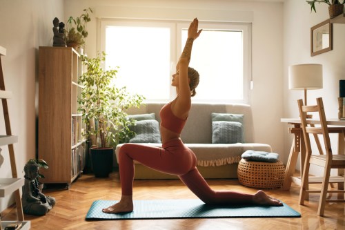 image of a person doing a low lunge yoga pose in a pink sports bra and matching leggings on their blue yoga mat in the middle of their living room, learning the best yoga poses for your zodiac sign