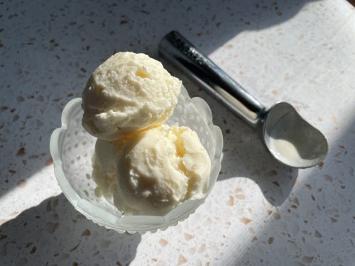 Two scoops of frozen yogurt in a glass dish on a marble countertop.