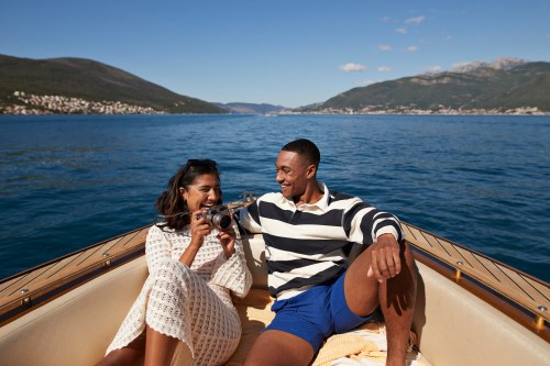 Happy young woman sitting with camera by boyfriend in motorboat on sea during sunny day