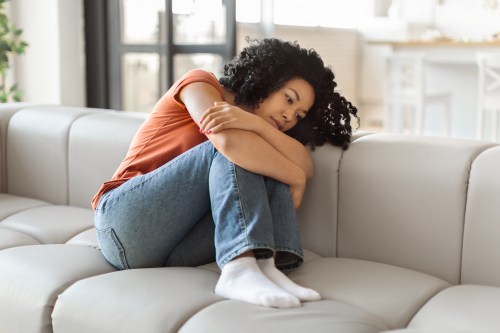 young woman in orange shirt sitting on couch crouching on legs