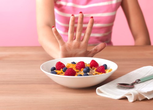 a female hand pushing away a bowl of cereal and berries