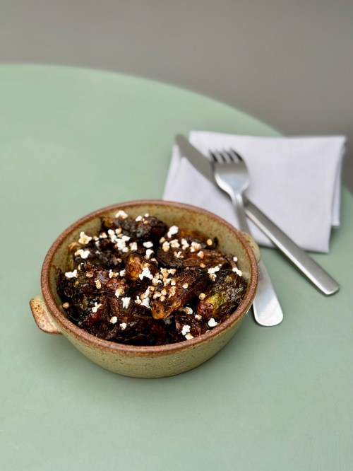 a plate of brussels sprouts in a small bowl on a green table
