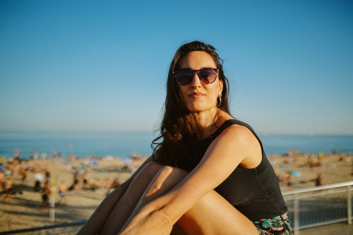 person sitting on a ledge outside during sunset wearing sunglasses overlooking the water