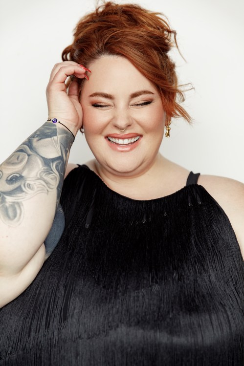 Model and Author Tess Holliday posing for the camera and smiling with her eyes closed while wearing a fringy black dress