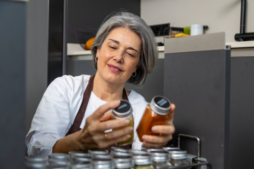 close up of person with short grey hair wearing a white shirt and a black apron looking through their spice cabinet to see if they have cinnamon which may cause medication interactions according to a new study