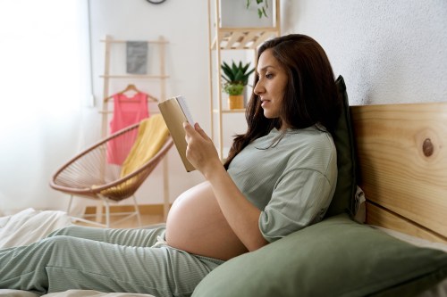 Pregnant woman enjoying reading a book while relaxing on bed at home. Pregnancy concept.